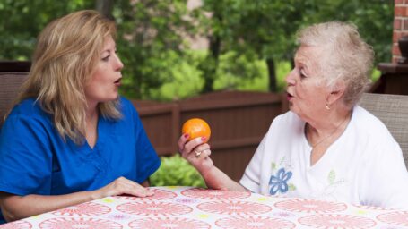 Speech therapist with female stroke patient outdoors during a home health therapy session modeling the production of a consonant during speech training for apraxia