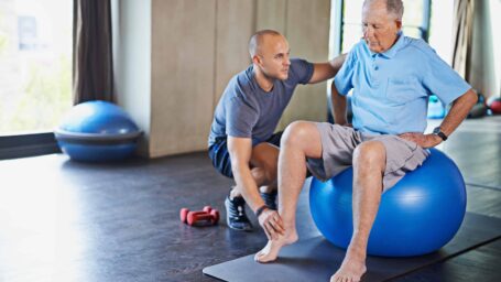 Physical therapist helps an elderly man on a yoga ball