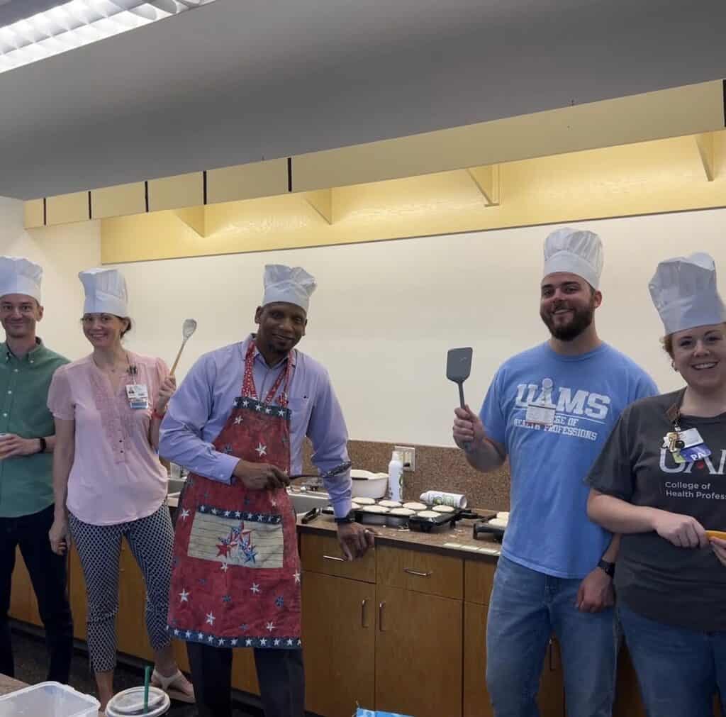 Members of the PA faculty stand with chef hats on and cooking utensils in their hands