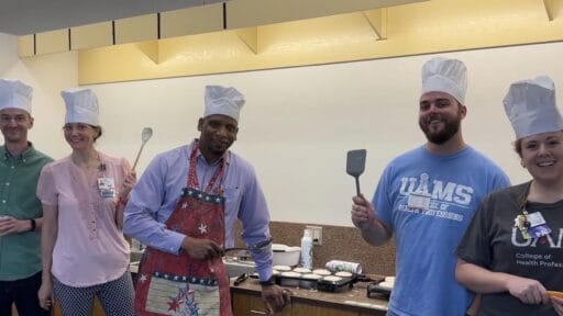 Members of the PA faculty stand with chef hats on and cooking utensils in their hands