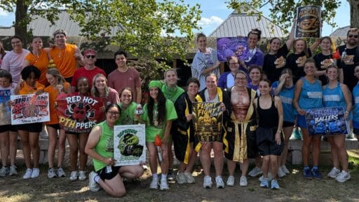 A group of Physician Assistant students posing outside with signs and uniforms