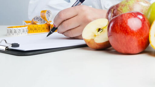 A person writing on a clipboard with a tape measure and apples near by