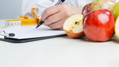 A person writing on a clipboard with a tape measure and apples near by