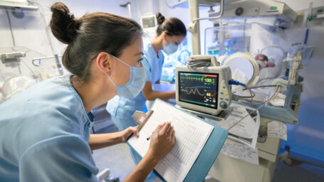 Nurse monitoring a premature newborn in an incubator while wearing a facemask