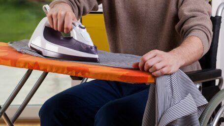 A person in a wheelchair ironing a shirt on an ironing board