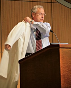 Keynote speaker UAMS Chancellor Dan Rahn, M.D., slips on his own white coat while talking about the symbolism and importance of the white coat in health care.
