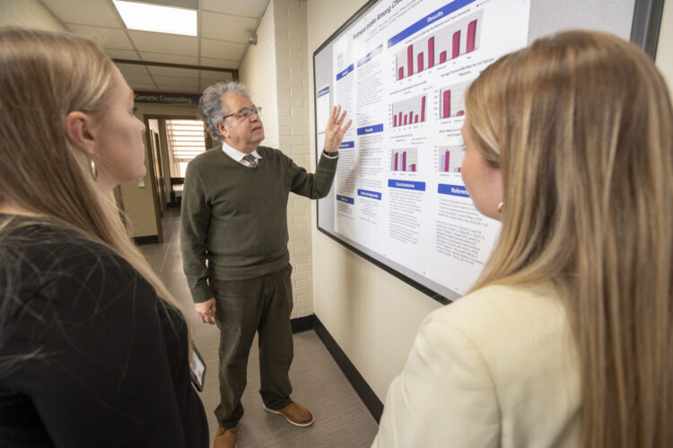 A professor shows a research poster to two female students