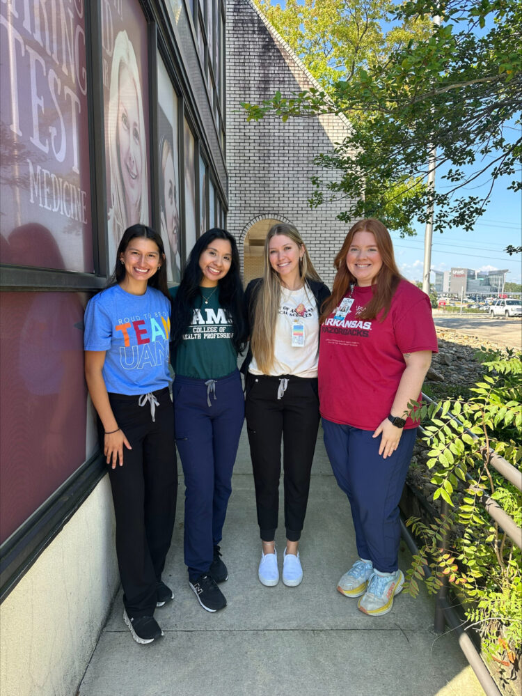 Four students standing together posing for the photo in UAMS shirts